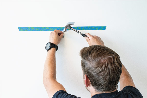 Hammering in a nail to a marked location on a wall.