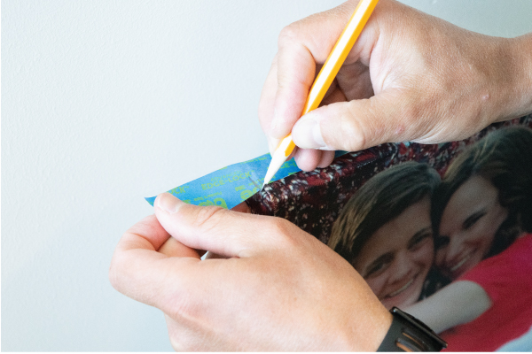 Marking painters tape with pencil at edge of canvas print.