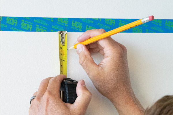 Marking a point on a wall using painters tape and tape measure as a guide.