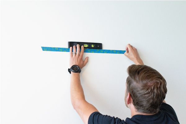 Person placing tape on wall using a spirit level to align it.