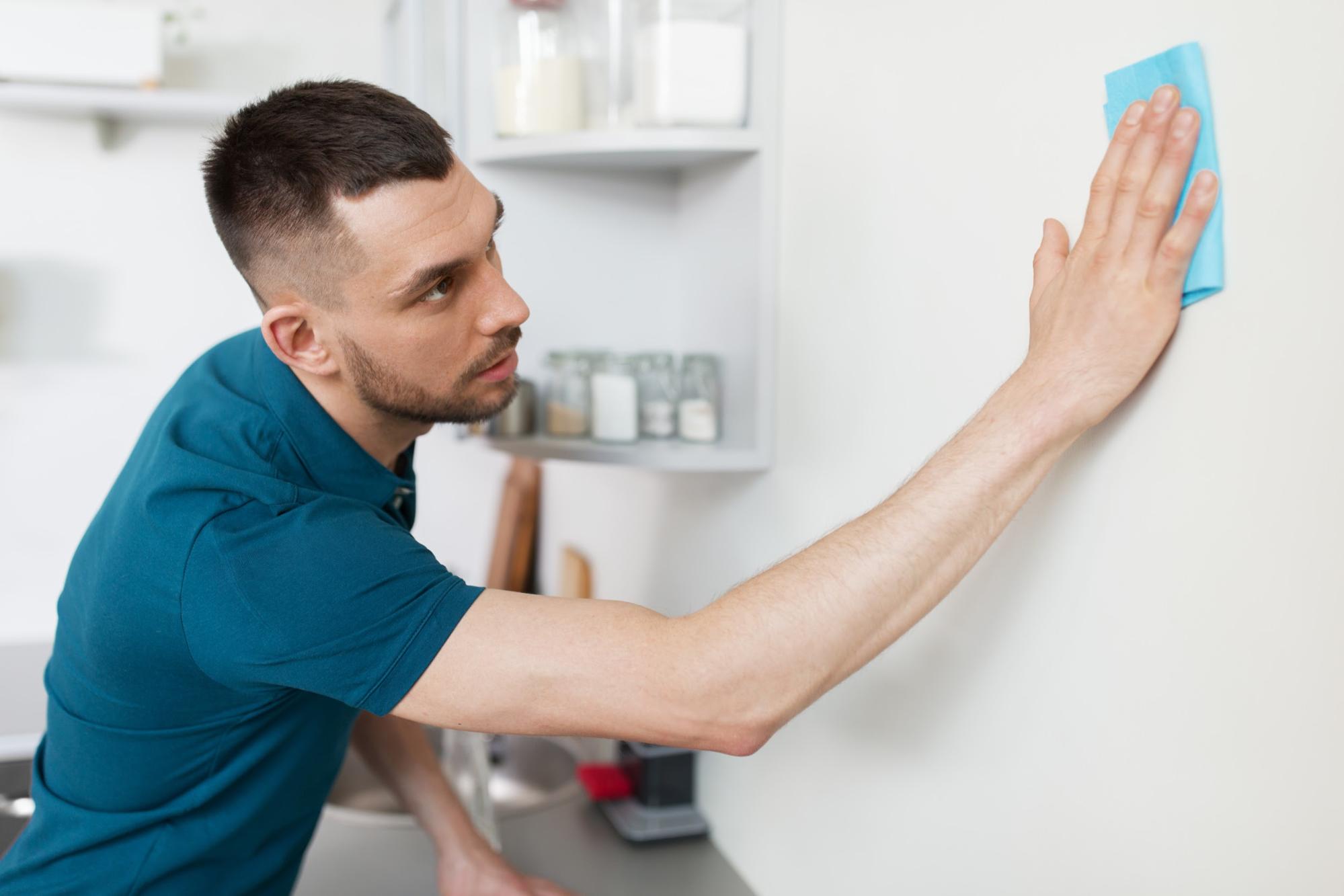 Man cleaning wall in home kitchen with blue microfiber cloth