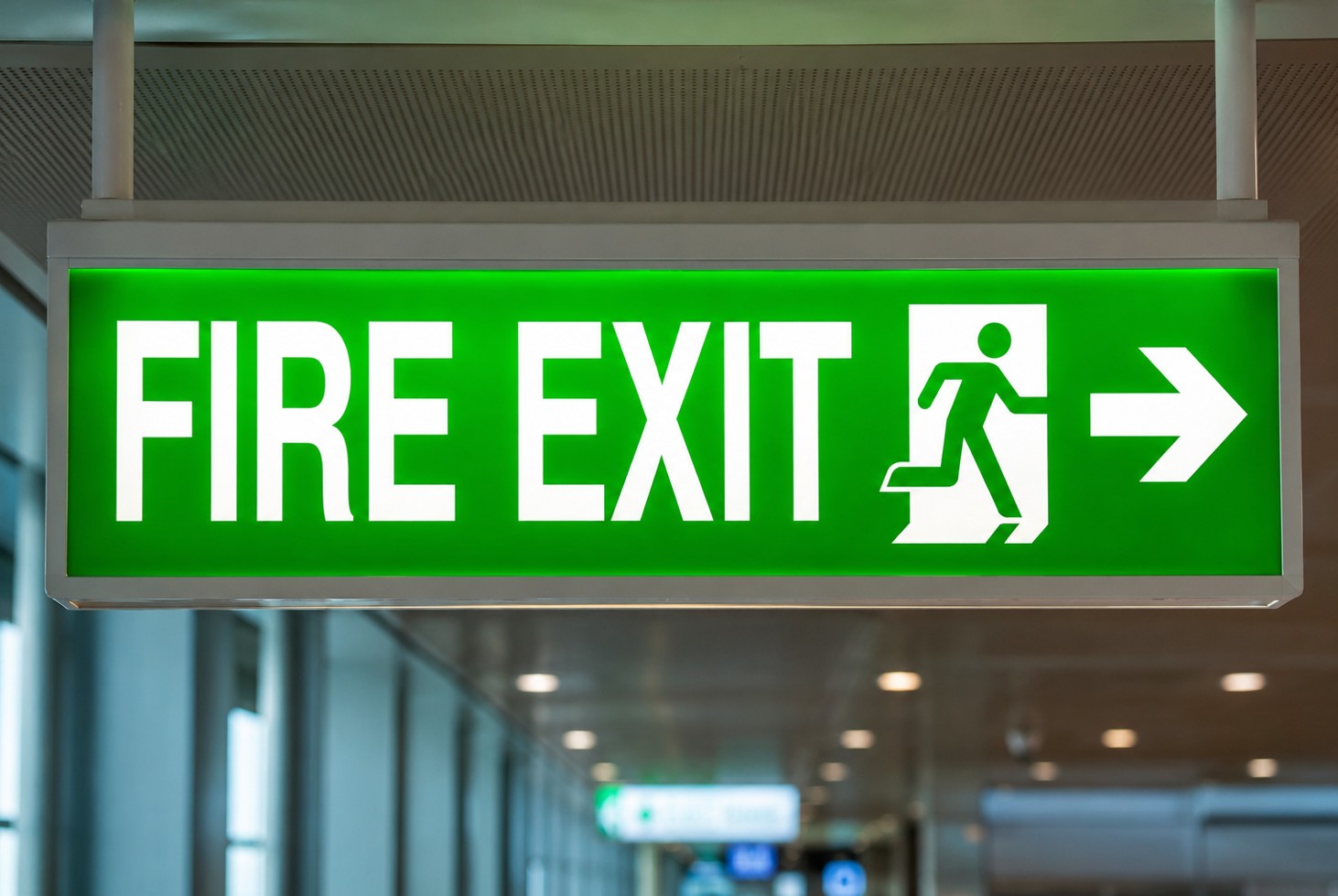 Green “FIRE EXIT” sign with arrow and running figure hanging inside a building.